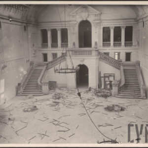 duży hol z monumentalnymi schodami, wysokim przeszklonym sklepieniem i dekoracjami; na podłodze widać uszkodzone elementy wnętrza, zerwany żyrandol