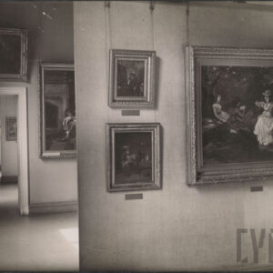 przestronna sala z obrazami zawieszonymi na linkach pod sufitem; na pierwszym planie duży obraz z trzema kobietami w kapeluszach i sukniach siedzącymi w ogrodzie, obok mniejsze portrety i sceny rodzajowe, po lewej otwarty korytarz z przejściem do kolejnych sal