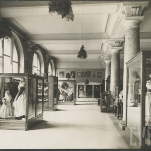 duża sala z eksponatami ludowymi i strojami regionalnymi w przeszklonych gablotach; widoczne manekiny w tradycyjnych strojach; arkadowe okna i kolumny z ozdobnymi kapitelami