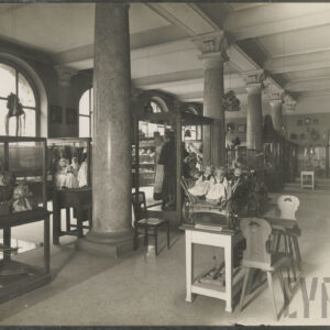 duża sala z eksponatami ludowymi i strojami regionalnymi w przeszklonych gablotach; widoczne manekiny w tradycyjnych strojach; arkadowe okna i kolumny z ozdobnymi kapitelami