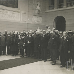 liczna grupa elegancko, odświętnie ubranych ludzi pozujących do fotografii, stojąc w dużym holu z ozdobnymi ścianami; widoczne rzeźby
