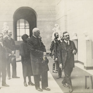 grupa elegancko ubranych osób w monumentalnym holu z ozdobnymi ścianami; widoczne rzeźby