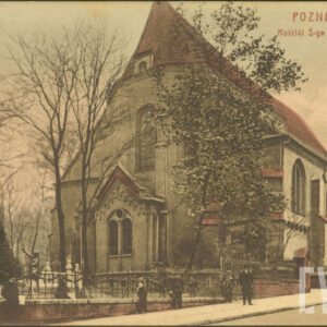 budynek sakralny ze spadzistym dachem i niższą nawą boczną, z lewej pomnik mężczyzny na cokole, otoczony kutym płotem na murowanej podmurówce