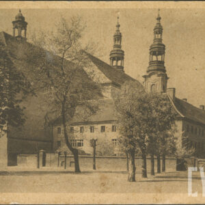 dwukondygnacyjny budynek z wysokim dachem na planie czworoboku, w głębi budowla sakralna z dwiema wysokimi barokowymi wieżami, na pierwszym planie drzewa