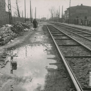 ulica z torami tramwajowymi w jezdni, obok torów wielkie kałuże i stosy kostki brukowej