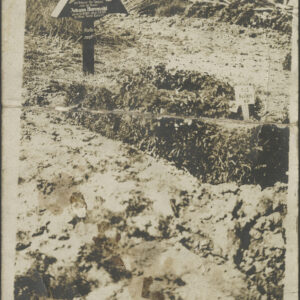 mogiła zwieńczona trójkątnym drewnianym krzyżem, wokół nierówna, poryta ziemia, z tyłu fragmenty drewnianego ogrodzenia