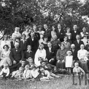 liczna grupa elegancko ubranych ludzi w różnym wieku, pozujących do fotografii na tle drzew 