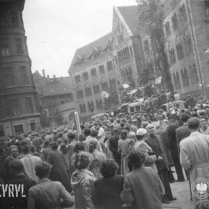 bardzo duża grupa ludzi zgromadzona na ulicy, pośrodku samochód ciężarowy z megafonami, na nim stoją ludzie, część trzyma flagi, w głębi monumentalny budynek