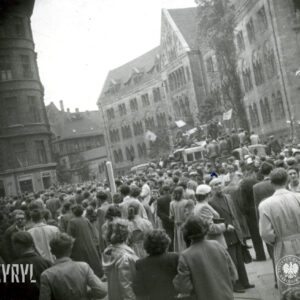 bardzo duża grupa ludzi zgromadzona na ulicy, pośrodku samochód ciężarowy z megafonami, na nim stoją ludzie, część trzyma flagi, w głębi monumentalny budynek
