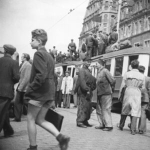 duża grupa ludzi stojąca na dachu tramwaju oraz wokół niego, w głębi okazały budynek