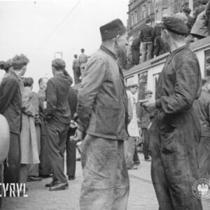 grupki stojących na ulicy ludzi, w głębi tramwaj, na jego dachu stoją ludzie
