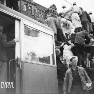 kilka osób wchodzi na dach tramwaju, część stojących im pomaga