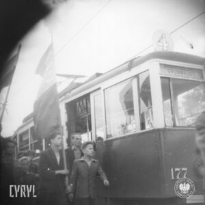 nastoletni chłopcy idą obok wagonu tramwajowego, jeden z nich trzyma flagę