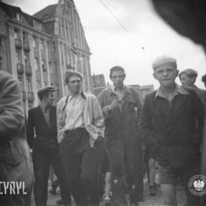 grupa młodych mężczyzn idzie ulicą, z prawej chłopiec, w głębi budynki