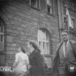 dwie kobiety i mężczyzna w płaszczu przed budynkiem