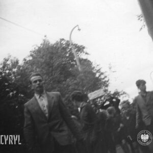 kilku mężczyzn, wśród nich chłopcy idą ulicą, w głębi drzewa
