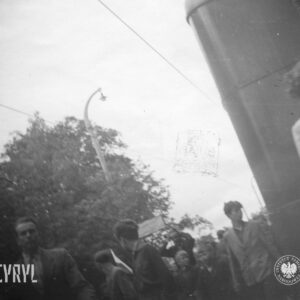 bardzo niewyraźne zdjęcie, grupa ludzi, wśród nich chłopcy, idą ulicą, z prawej fragment samochodu