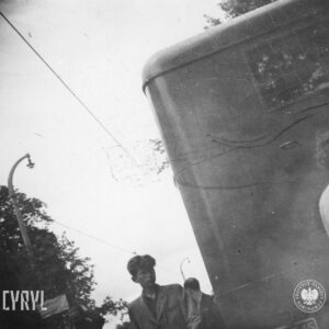 bardzo niewyraźne zdjęcie, grupa ludzi, wśród nich chłopcy, idą ulicą, z prawej fragment samochodu
