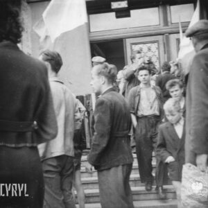 grupa ludzi schodzi po schodach prowadzących do budynku, kilka osób trzyma flagi