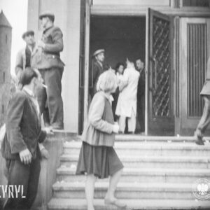 grupki osób na schodach, przed wejściem i za drzwiami wejściowymi budynku