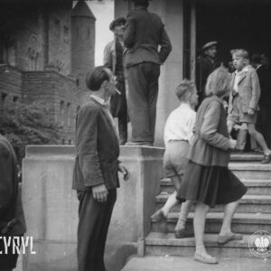 grupki osób na schodach, przed wejściem i za drzwiami wejściowymi budynku