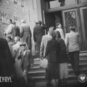 grupa osób przed wejściem i na schodach prowadzących do budynku, w głębi okazały budynek