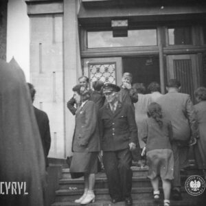 grupa kobiet i mężczyzn wchodzi po schodach do budynku, w głębi otwarte drzwi do budynku