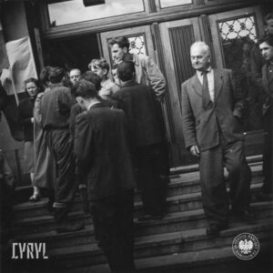 grupa ludzi przed wejściem do budynku, część wchodzi po schodach lub z nich schodzi, w głębi otwarte drzwi do budynku