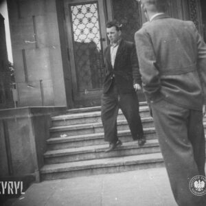 dwóch mężczyzn przed wejściem do budynku, jeden z nich schodzi po schodach