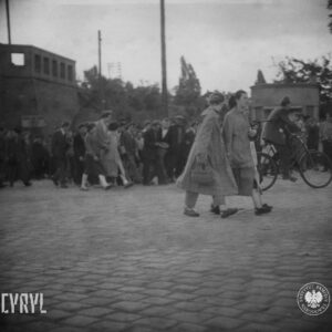 duża grupa ludzi zgromadzona na skrzyżowaniu brukowanych ulic, w głębi murowany element architektoniczny wiaduktu