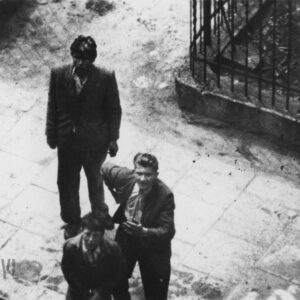 dwóch młodych mężczyzn i chłopiec sfotografowani od góry, prawdopodobnie z okna budynku,  stoją przy metalowym ogrodzeniu