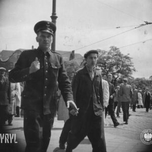 duża grupa ludzi, przeważnie mężczyzn idzie ulicą, na pierwszym planie mężczyzn w mundurze kolejowym, w głębi budynek