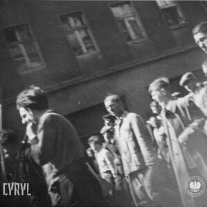duża grupa ludzi idzie ulicą, w głębi fragment budynku