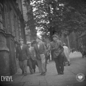 kilku mężczyzn idzie chodnikiem, po obu stronach ulicy zabudowania