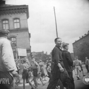 ludzie idący ulicą, część w kombinezonach roboczych