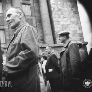 grupa mężczyzn idzie ulicą, w głębi okazały budynek