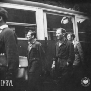 kilku młodych mężczyzn, część w roboczych ubraniach, na tle wagonu tramwajowego