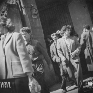 grupa ludzi przed bramą do kamienicy, z lewej widoczny postrzępiony mur