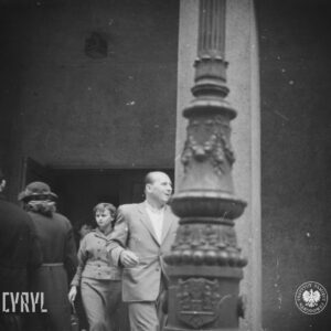 kilka osób wychodzi z budynku, na pierwszym planie fragment bogato zdobionej latarni