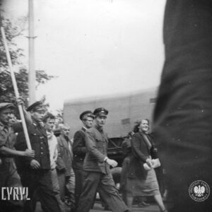 grupa ludzi idzie ulicą, wśród nich trzech mężczyzn w mundurach