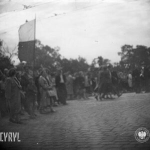 duża grupa ludzi idzie całą szerokością brukowanej ulicy, jedna osoba trzyma flagę