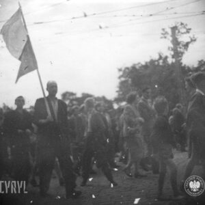 duża grupa ludzi idzie całą szerokością brukowanej ulicy, jedna osoba trzyma flagę