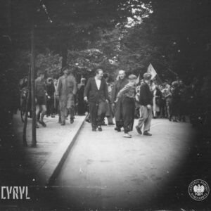 grupa ludzi idzie ulicą, w głębi drzewa, brzegi zdjęcia czarne