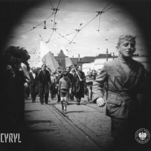 duża grupa ludzi idzie brukowana ulicą, kilka osób trzyma flagi, wyraźnie widoczna czarna obwódka wokół zdjęcia