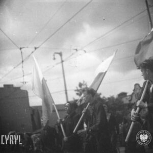 duża grupa ludzi idzie ulicą, kilka osób na ramionach niesie flagi 