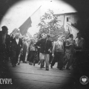 grupa ludzi idzie ulicą, kilka osób trzyma polskie flagi, fotografia ma wyraźną czarną otoczkę