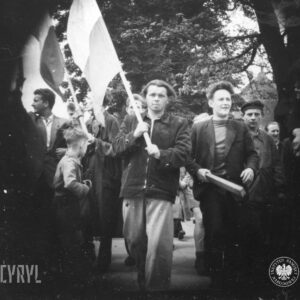 duża grupa przeważnie młodych mężczyzn, kilku z nich trzyma w rękach polskie flagi na drzewach, w głębi drzewa