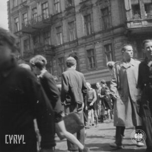 duża grupa ludzi na ulicy, większość idzie środkiem, w głębi narożna kamienica