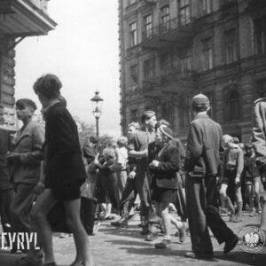 duża grupa ludzi na ulicy, większość idzie środkiem, po obu stronach ulicy kamienice