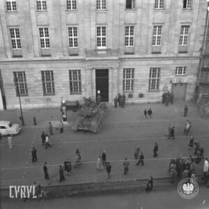 czołg stojący przed okazałym budynkiem, pod ścianą budynku kilku żołnierzy wokół pojedynczy ludzie